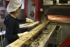 Woman puts fresh pretzels into the oven.