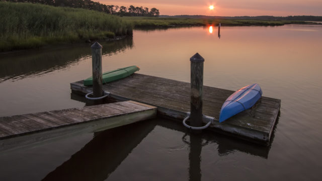 Light pink sunset showing dock with two kayaks in the foreground.